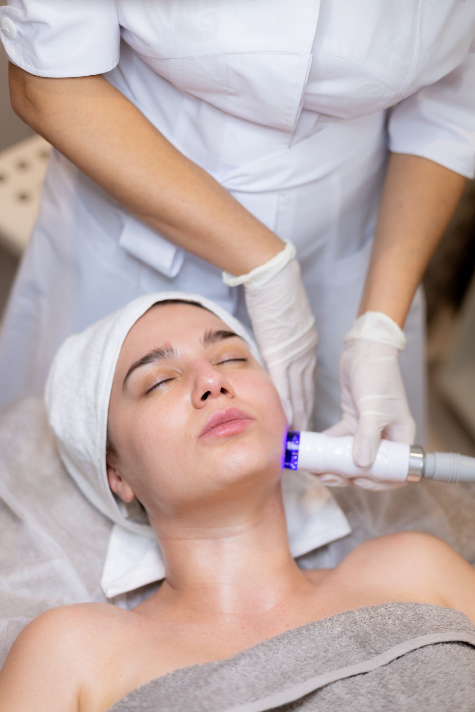 A young beautiful girl lies on the beautician's table and receives procedures with a professional apparatus for skin rejuvenation and moisturizing