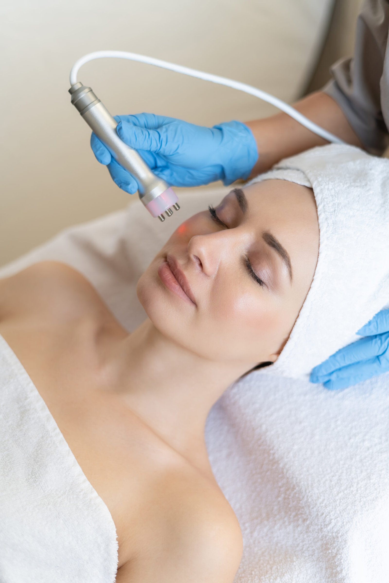 Young woman lying on cosmetologist's table during rejuvenation procedure. Cosmetologist take care about neck and face skin youthfull and wellness. Hardware face cleaning procedure